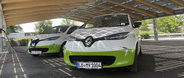Zwei my-e-car-Fahrzeuge von NaturEnergie stehen nebeneinander unter einem Photovoltaik-Dach