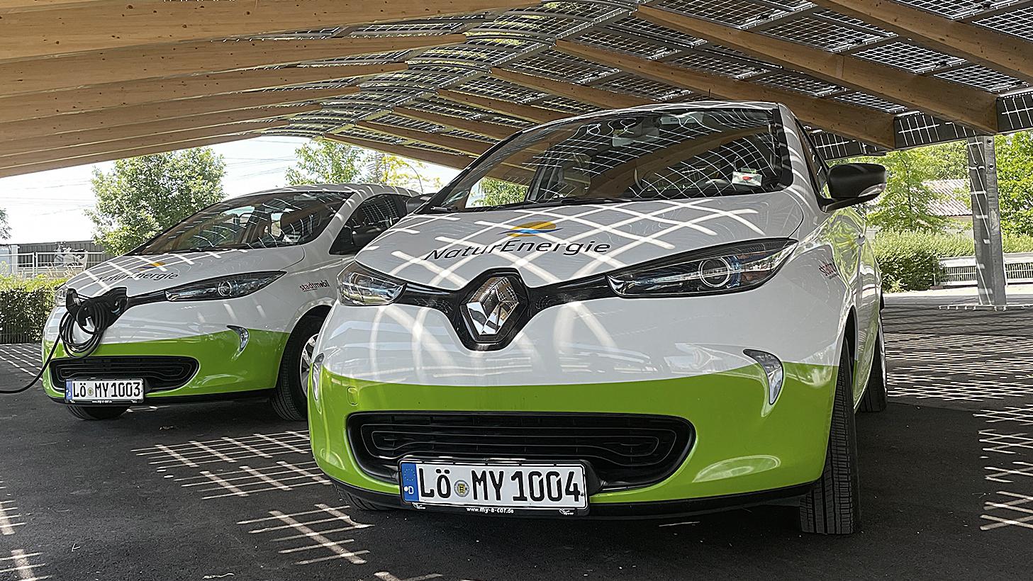 Zwei my-e-car-Fahrzeuge von NaturEnergie stehen nebeneinander unter einem Photovoltaik-Dach