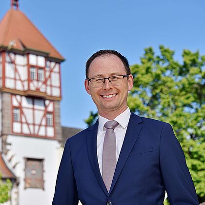 Bürgermeister Bächle im Anzug vor einem historischen Fachwerkgebäude.