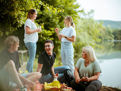 Eine Gruppe von fünf Personen bei einem Picknick am Seeufer.