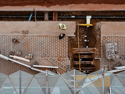 Blick von oben auf eine Baustelle mit geöffneten Leitungsgräben und verlegten Versorgungsrohren.