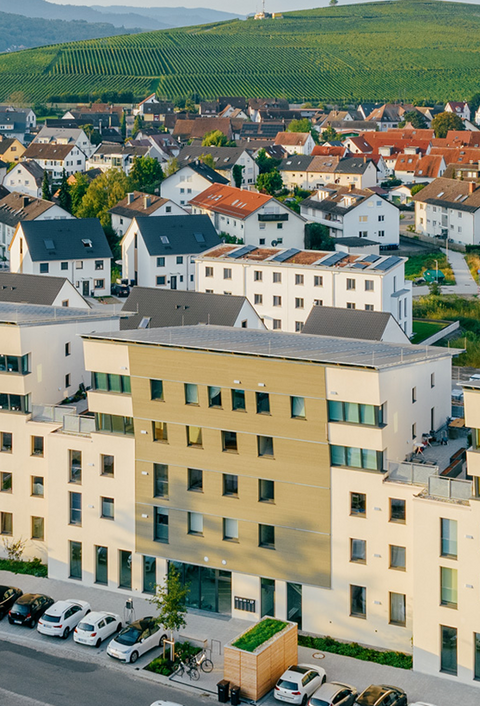 Luftaufnahme einer modernen Wohnüberbauung mit Photovoltaikanlagen und umliegender Landschaft.