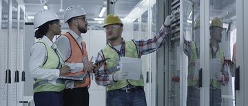 Gruppe Männer und Frauen Solaranlagenkontrollzentrum Gruppe multiethnischer Männer und Frauen in Hardhats, die in der Halle des Solaranlagenkontrollzentrums tätig sind, diskutiert zwischen Racks