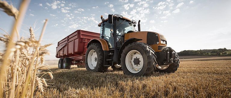 Ein Traktor mit Anhänger steht auf einem Feld bei schönem Wetter und blauem Himmel