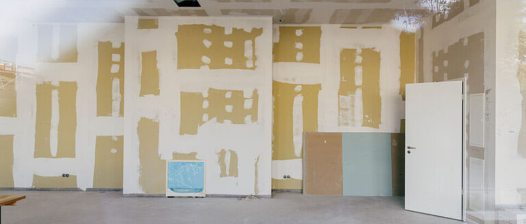 Unfertiger Innenraum mit verspachtelten Trockenbauwänden und geöffneter Tür.