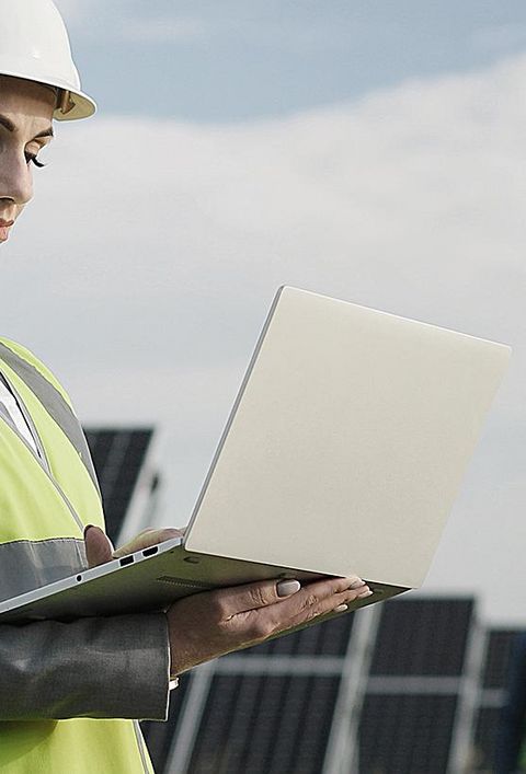 Elektroingenieurin in Schutzhelm und Uniform mit Laptop prüft Solarpaneele. 