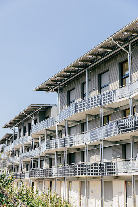 Modernes Gebäude mit Balkonen und strukturierter Fassade vor blauem Himmel