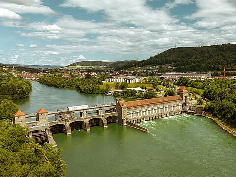 Flusslandschaft mit Staudamm und Stadt im Hintergrund Fluss mit Staudamm, roten Dächern und Stadt im Hintergrund