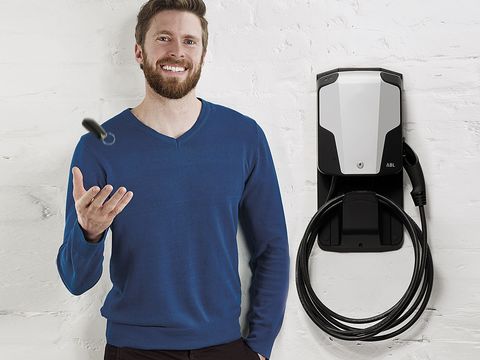 Ein Mann mit blauem Pullover steht vor einer ABL Wallbox für Elektroautos und wirft seinen Autoschlüssel in die Luft.