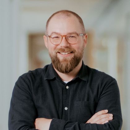 Daniel Moll, Application Administrator, steht mit verschränkten Armen in einem modernen Büroflur.