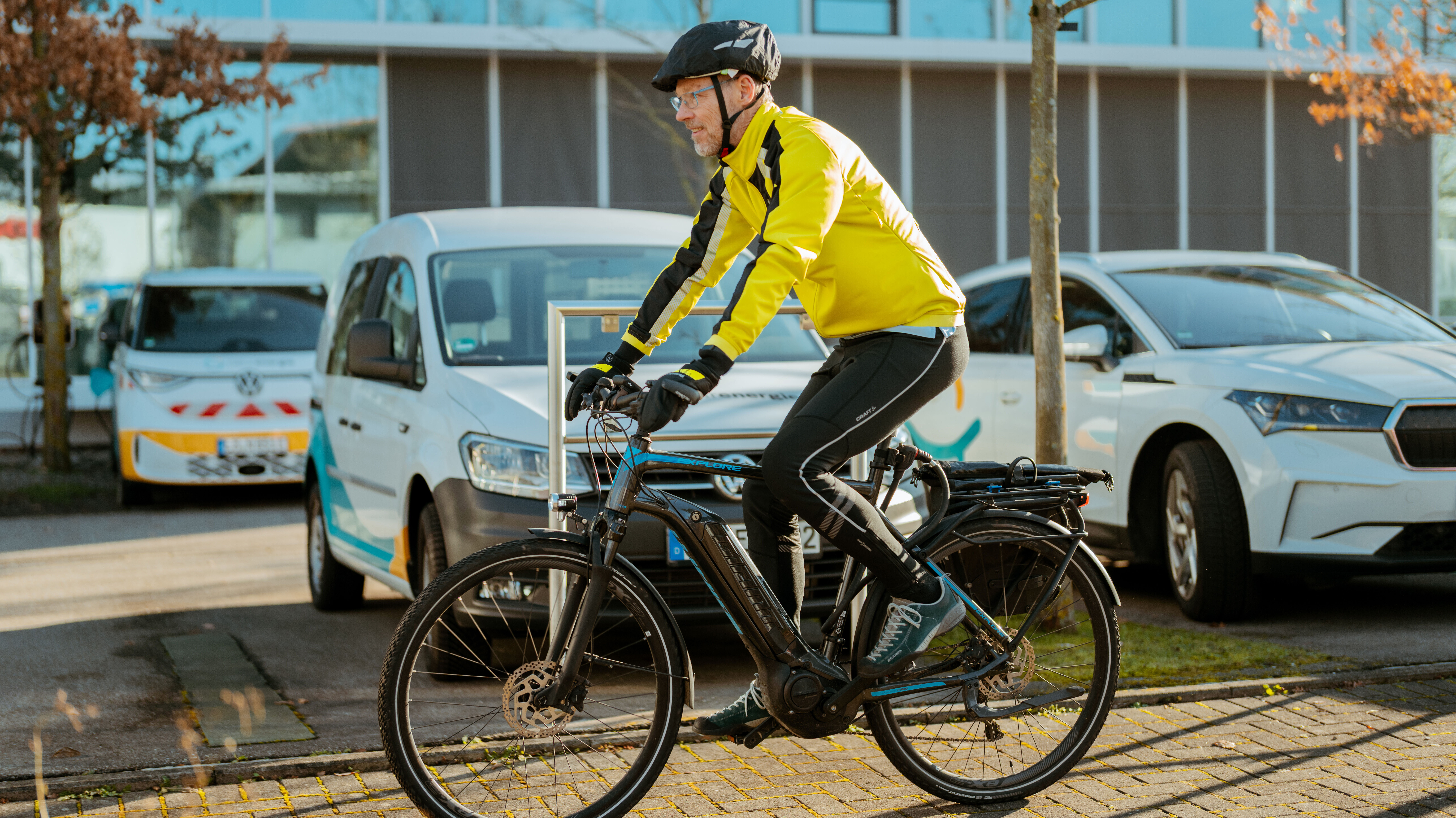 naturenergie Standort Südbaden. Ein Mitarbeiter fährt mit dem Fahrrad am Firmenparkplatz entlang.