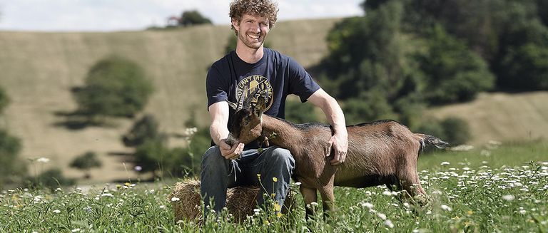 Florian Burkhard vom Lindenhof mit einer Ziege im Arm auf einer Wiese. Landwirtschaft im Schwarzwald.