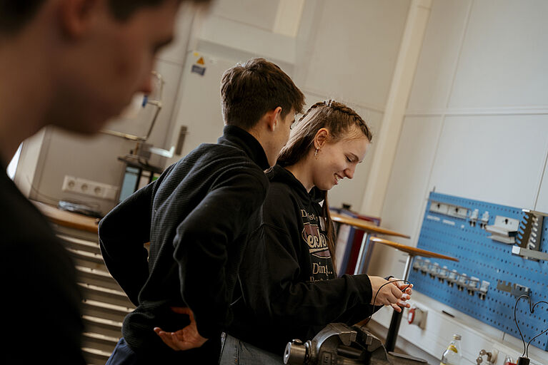 Drei Personen in einer Werkstatt mit Werkzeugwand und Werkbank