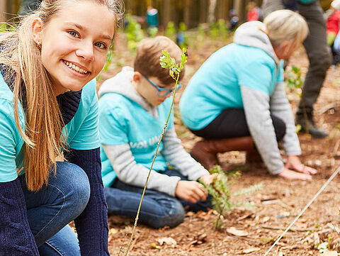 Freiwillige Kinder pflanzen Bäume am Waldrand in herbstlicher Stimmung.