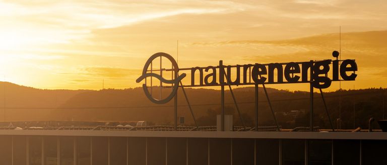 Das Bild zeigt das naturenergie-Logo auf dem Dach des Hauptgebäudes in Rheinfelden bei Sonnenuntergang.