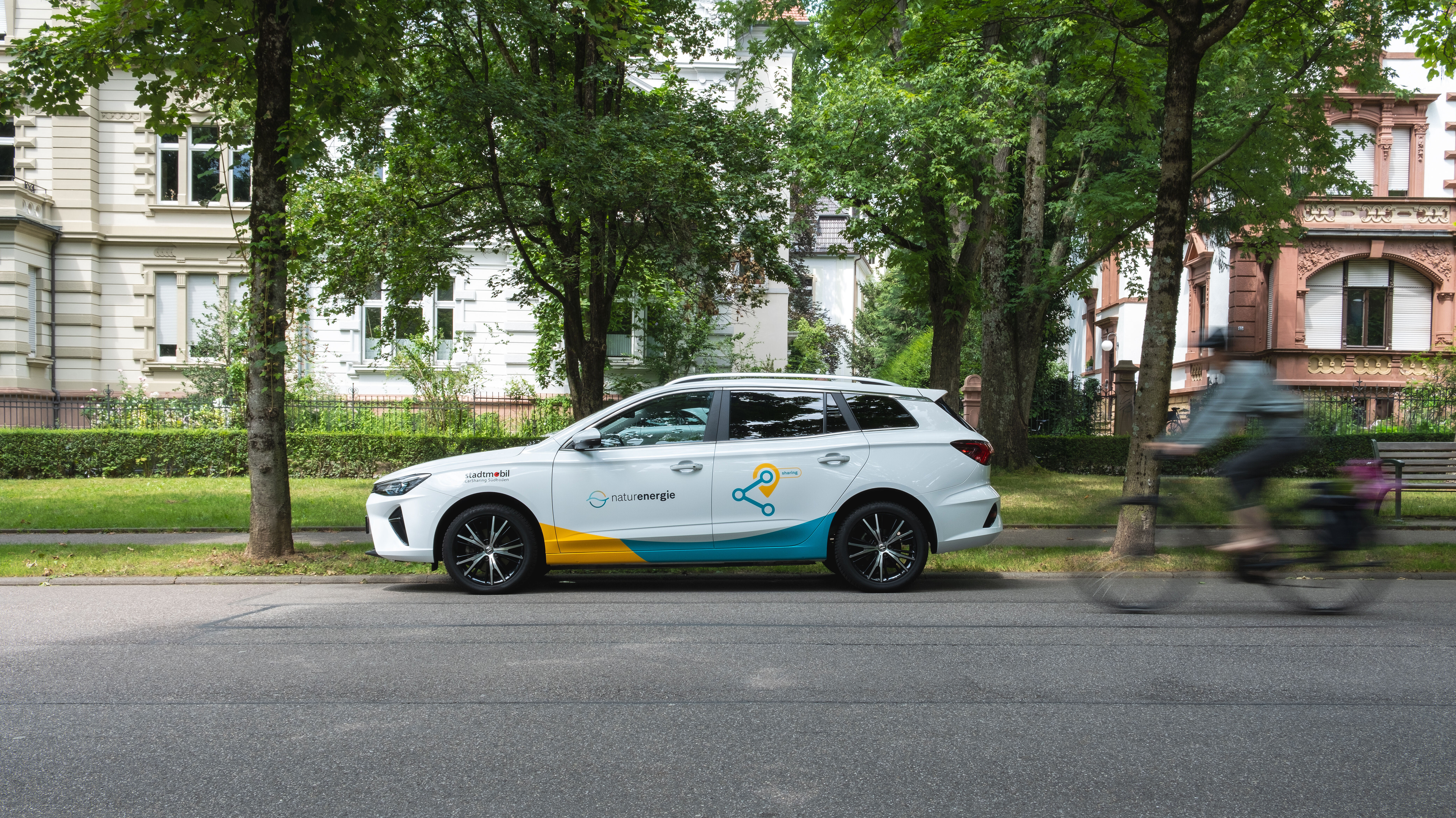 Geparktes Auto mit Carsharing-Beschriftung, Fahrradfahrer fährt vorbei