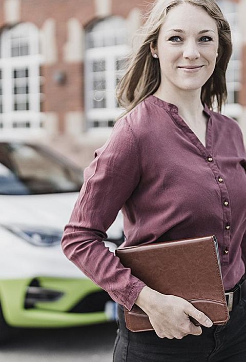 Eine Frau steht mit einer Mappe in der Hand vor einem Elektroauto von my-e-car