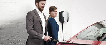 Mann und Frau vor ABL Wallbox Mann und Frau stehen vor einem roten Fahrzeug, Der Mann ist gerade dabei den Ladevorgang an einer ABL Wallbox zu starten.