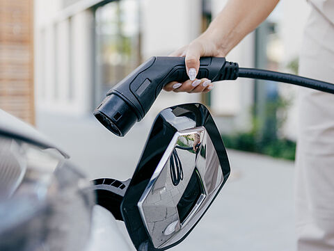 Ladekabel wird an Elektroauto angeschlossen Hand hält Ladekabel vor geöffnetem Ladeanschluss eines Elektroautos