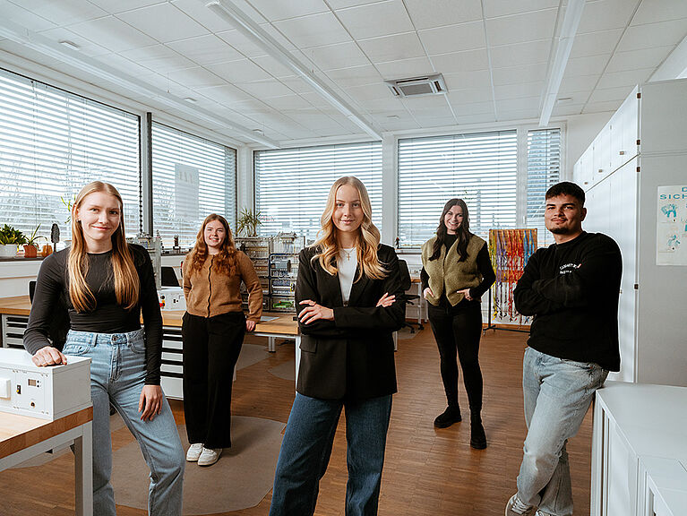 Mehrere Personen stehen gemeinsam in einem Arbeitsraum mit Geräten und Arbeitsflächen.