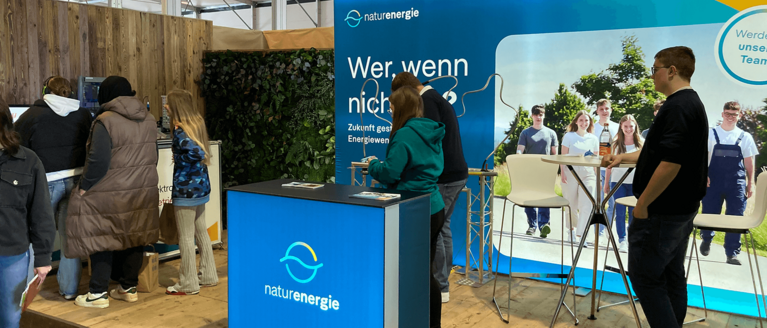 Messestand von naturenergie mit Infotresen, Werbewand und mehreren Personen