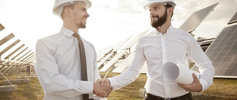 Fröhliche bärtige Männer mit Lächeln und Händeschütteln beim Abschluss einer Vereinbarung während der Arbeiten an einem Solarkraftwerk