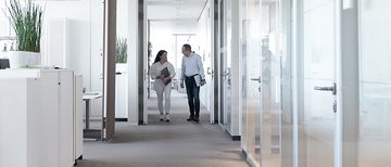 Zwei Energiedienst-Mitarbeiter unterhalten sich während sie laufen im Büro in Rheinfelden. Das Büro ist hell und es ist eine grüne Pflanze zu sehen.