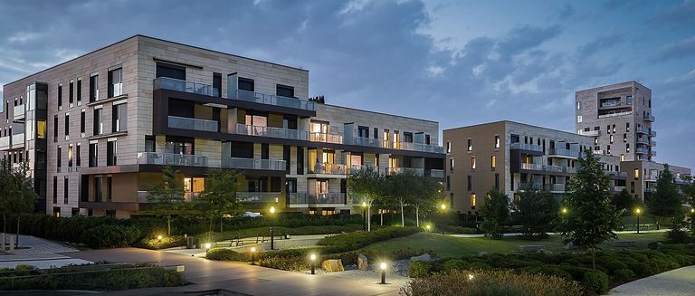 Grüner Park mit modernen Häusern im Hintergrund am Abend. Leuchtende Grünfläche mit Gras und Bäumen.