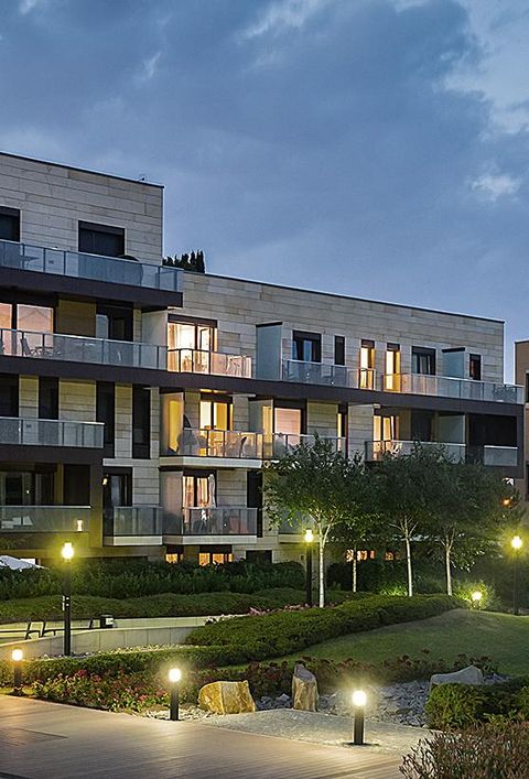 Grüner Park mit modernen Häusern im Hintergrund am Abend. Leuchtende Grünfläche mit Gras und Bäumen.