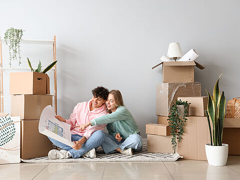 Junges Pärchen sitzt auf dem Boden zwischen Umzugskartons