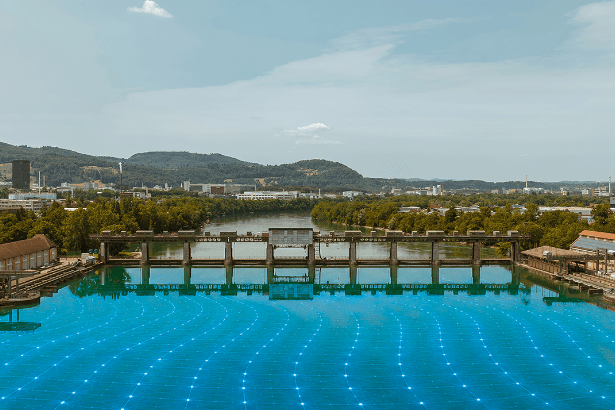 Blick auf ein Wasserkraftwerk mit Stauwehr und blau visualisiertem Energienetz auf der Wasseroberfläche.