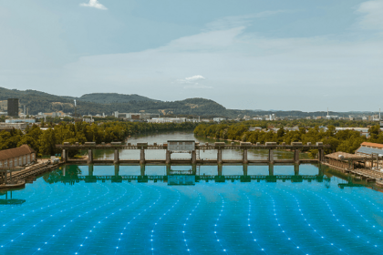 Blick auf ein Wasserkraftwerk mit Stauwehr und blau visualisiertem Energienetz auf der Wasseroberfläche.