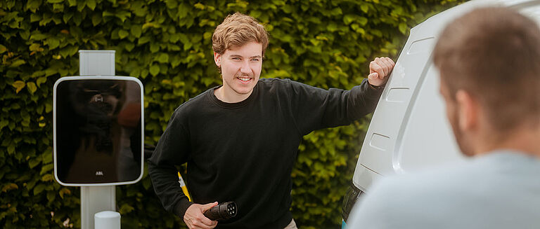 Ladevorgang an E-Fahrzeug Zwei Personen an einem weißen Van beim Ladevorgang an einer E-Ladestation