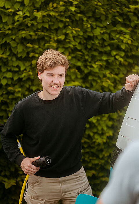 Zwei Personen an einem weißen Van beim Ladevorgang an einer E-Ladestation