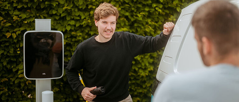 Zwei Personen an einem weißen Van beim Ladevorgang an einer E-Ladestation
