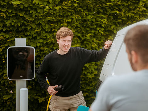 Zwei Personen an einem weißen Van beim Ladevorgang an einer E-Ladestation