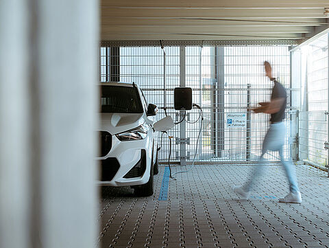  Weißes Elektroauto lädt an einer Wandladestation in überdachter Ladezone.