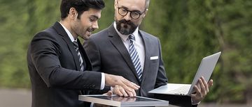 Geschäftsmann mit einem Solarpanel in der Hand und Ingenieur, der einen Laptop hält, unterhalten sich draußen in der Natur. 