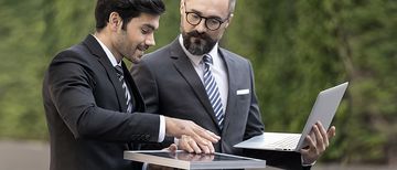Business Meeting Solar Geschäftsmann mit einem Solarpanel in der Hand und Ingenieur, der einen Laptop hält, unterhalten sich draußen in der Natur.