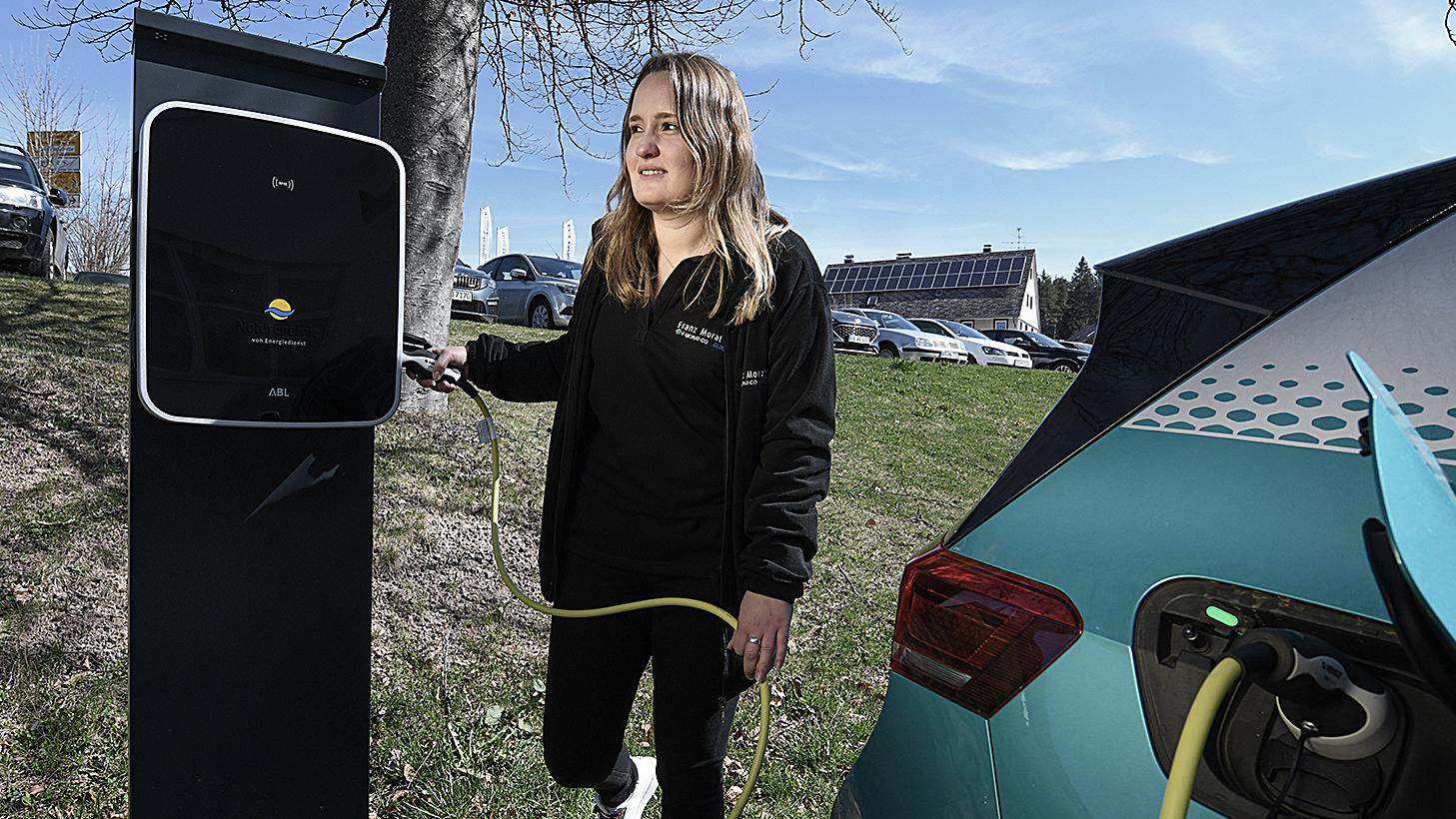 Frau lädt E-Auto an einer ABL Wallbox von NaturEnergie in ländlicher Umgebung