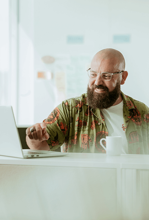 Zufriedener Mann mit Kaffee steht vor einem Laptop und zeigt einer anderen Person den Bildschirm