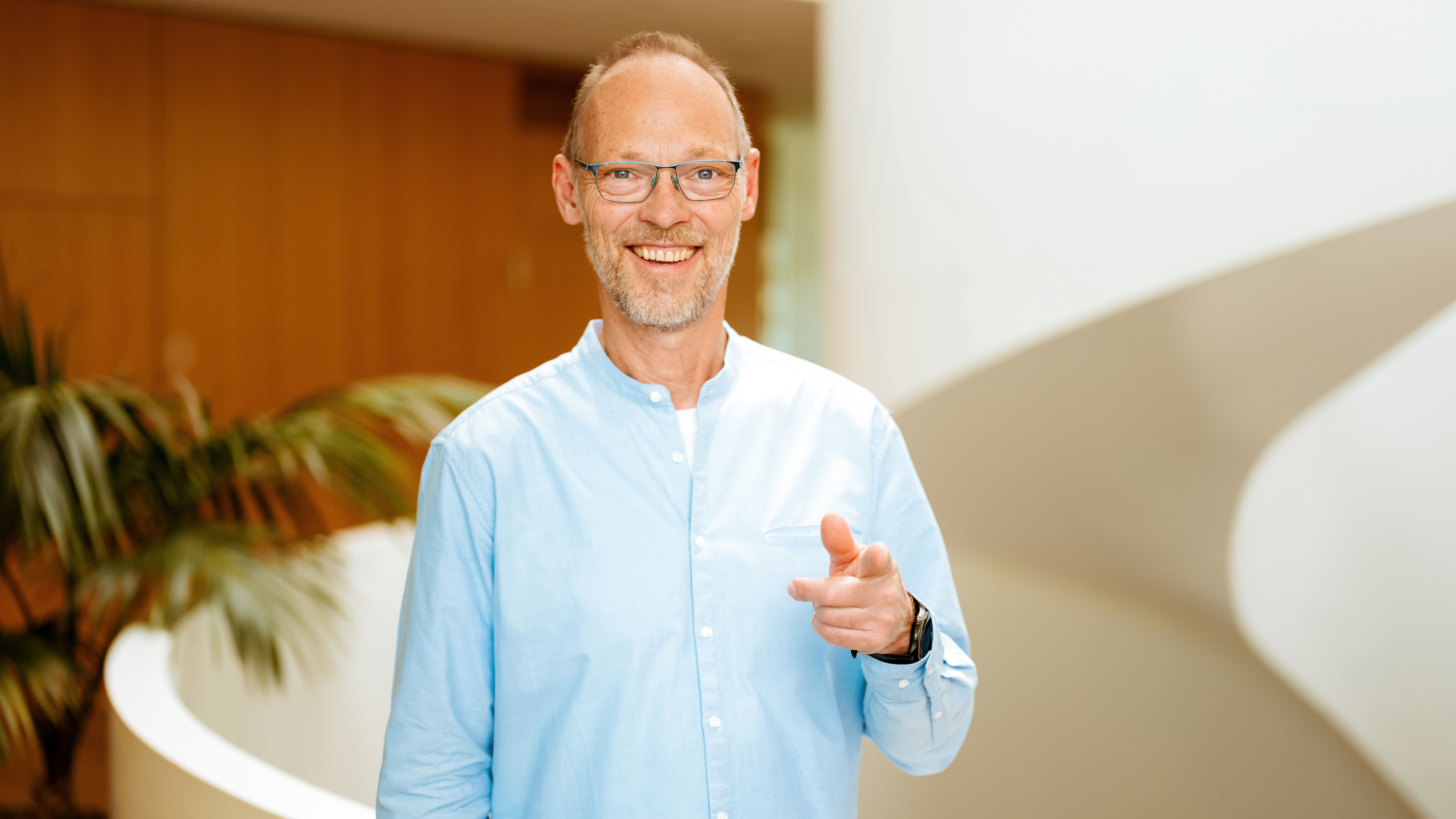 Person zeigt direkt in die Kamera und steht in einem modernen Innenraum als Einladung zur Energieberatung