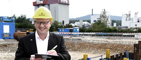 Leiter Bereich Wärme-und Energielösungen Nahwärme-Baustelle Evonik Leiter des Bereichs Wärme-und Energielösungen steht mit Schreibbrett und Bauhelm mitten auf einer Nahwärme-Baustelle mit Rohrleitungen vor dem Industriegebäude Evonik