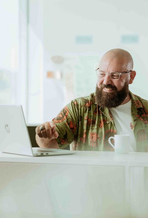 Zufriedener Mann mit Kaffee steht vor einem Laptop und zeigt auf den Bildschirm