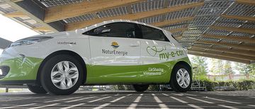 Ein my-e-car-Fahrzeug von NaturEnergie steht unter einem Photovoltaik-Dach
