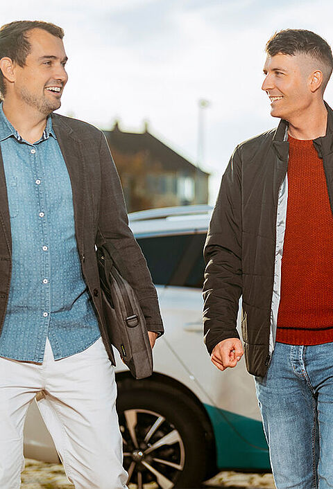 Zwei Personen gehen mit Unterlagen an einem naturenergie Fahrzeug vorbei.