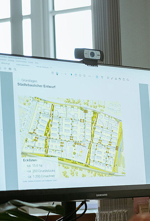 Eine Person sitzt am Schreibtisch und betrachtet einen städtebaulichen Entwurf auf einem Computerbildschirm.
