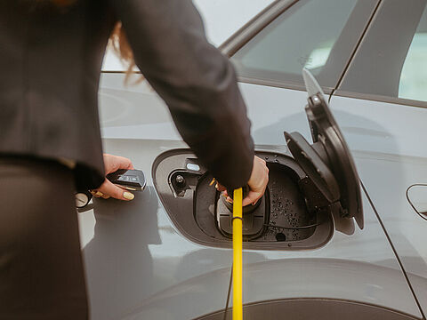 Gelbes Ladekabel wird in die Ladebuchse eines grauen Elektroautos gesteckt.