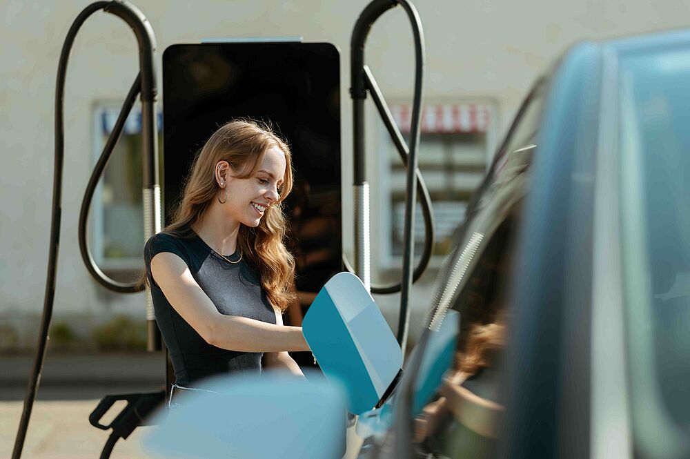 Person lädt Elektroauto an Ladestation vor Gebäude