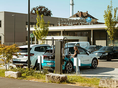 Zwei Elektroautos laden an einer Doppel-Ladesäule vor einem Firmengebäude.